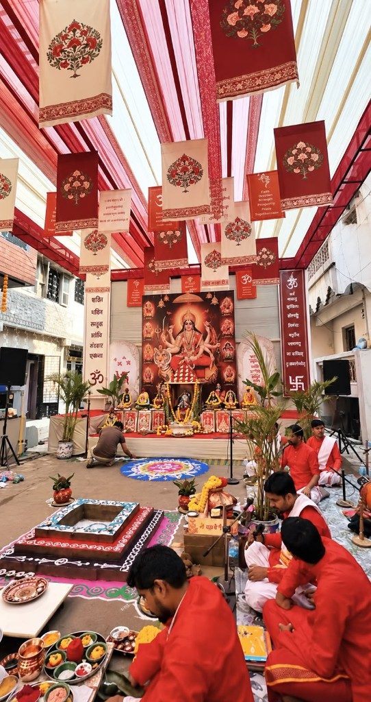 Ceremonial stage with red and cream drapes, banners and rangoli